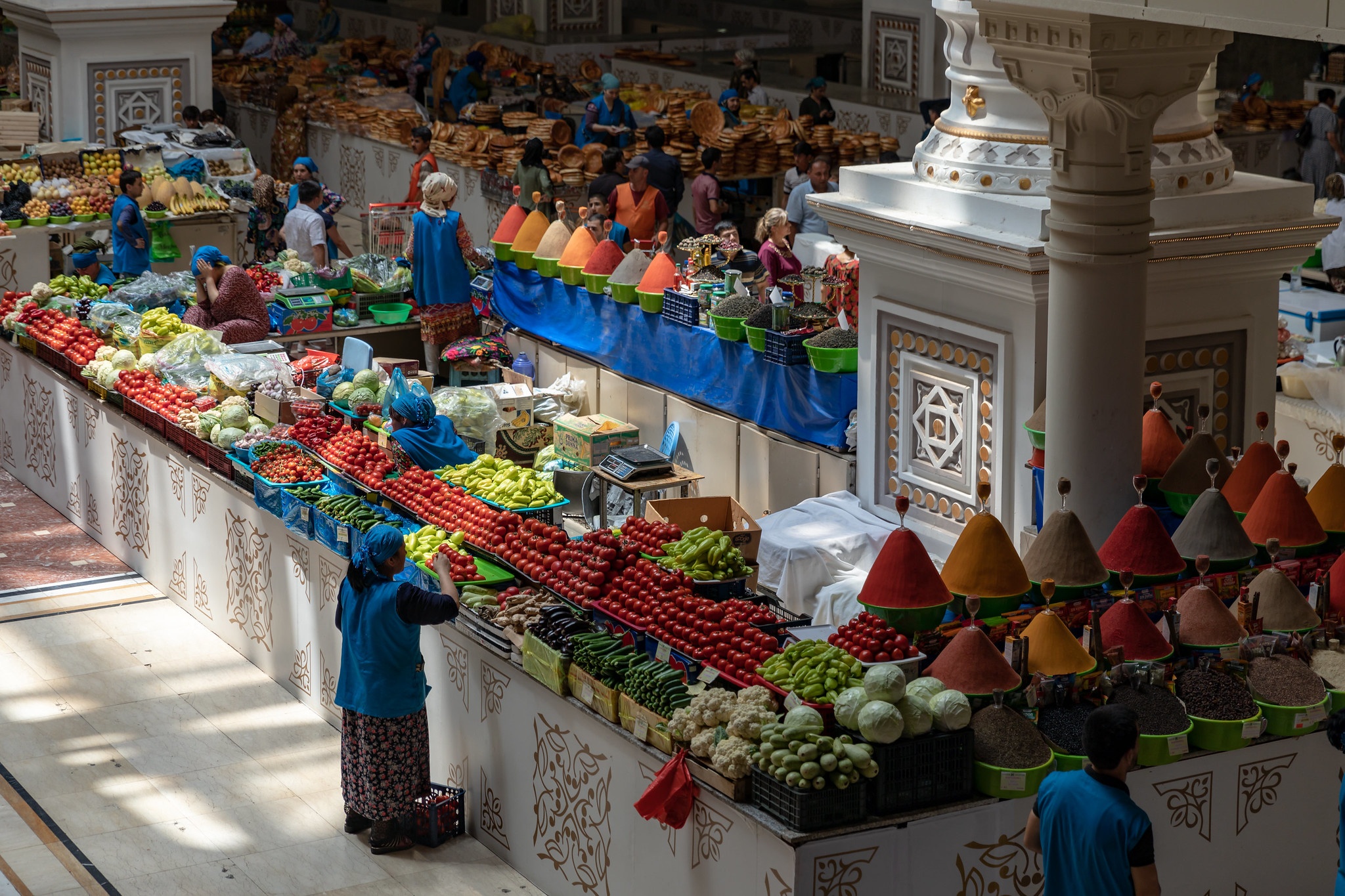 A woman is standing in front of a stall full of fruits at a bazar in Tajikistan