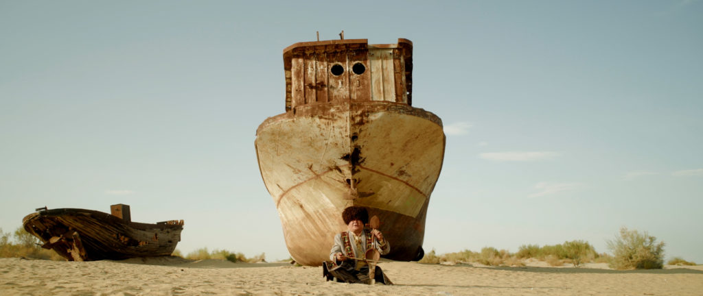 An Uzbek musician performs a traditional song. Behind him, the ship graveyard of Moynaq where the Aral Sea used to be. 