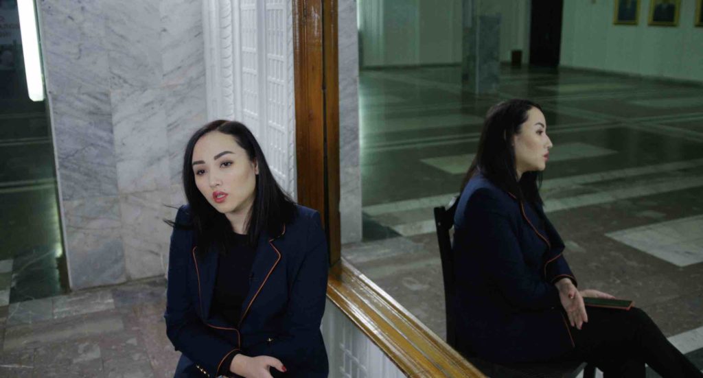 Still from the film The Wife: a woman sitting next to a mirror, talking.