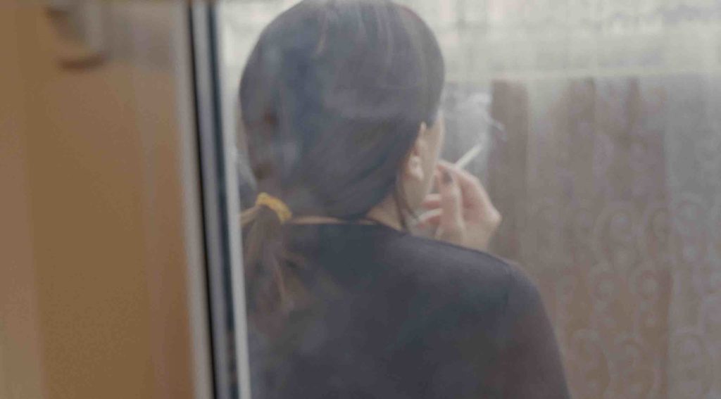 Still from the film The Wife: a woman smoking, seen from the back