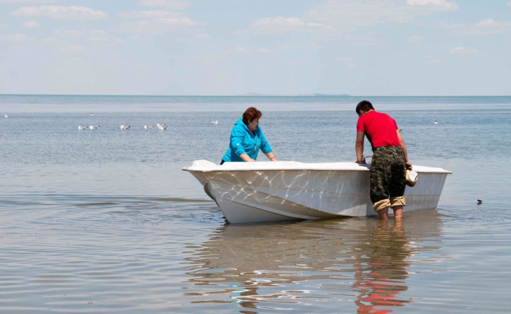 Two people pushing a small boat into the water in the Aral Sea region