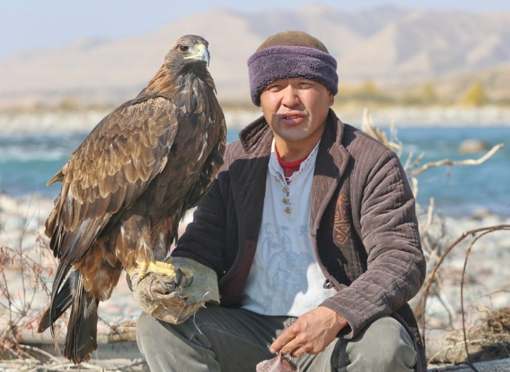 Aman Ismailov sitting by the river with one of his eagles