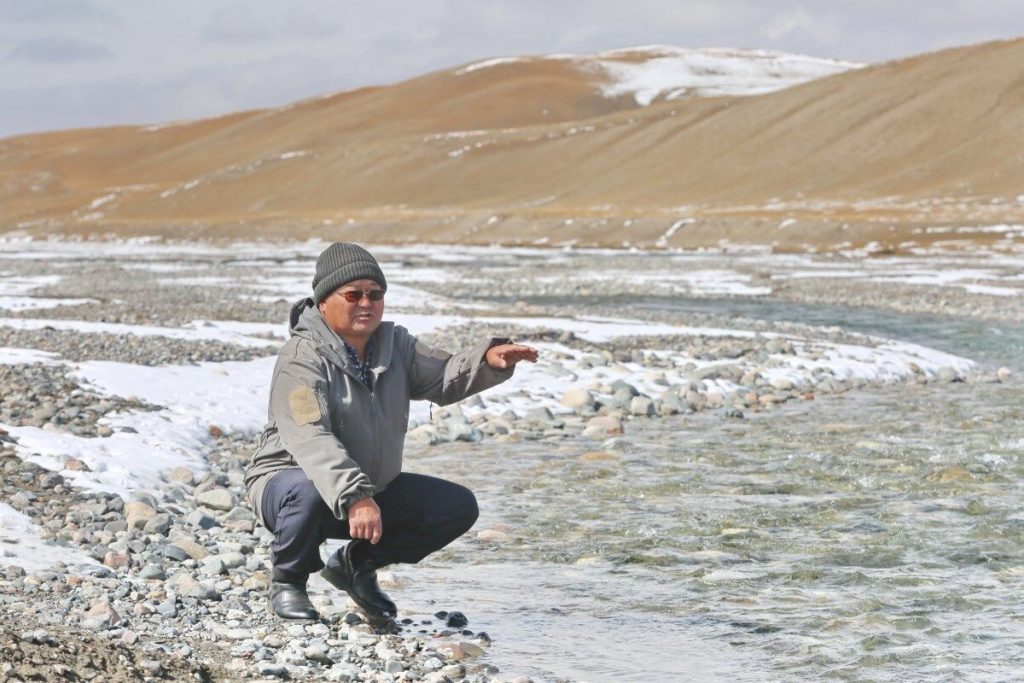 Satybaldy Imankulov squatting by the river, in the mountains.