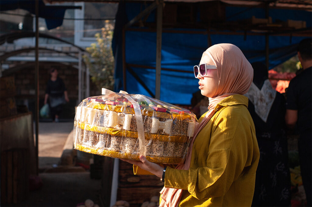 a young woman with glasses carrying a large tray of cakes.