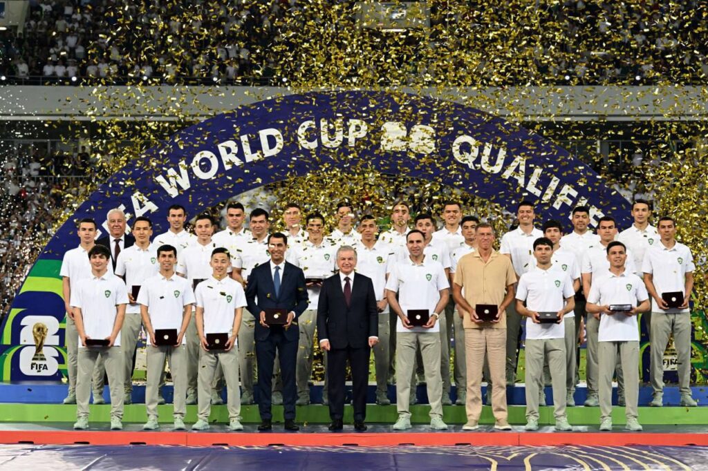 Le président ouzbek Chavkat Mirzioïev au milieu de l'équipe nationale de football, au stade Bunyodkor de Tachkent, après la qualificiation de l'Ouzbékistan au mondial 2026. Crédit : site web de la présidence.