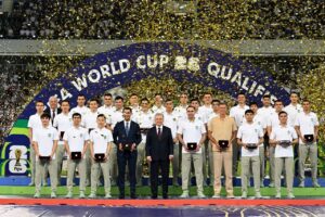 Le président ouzbek Chavkat Mirzioïev au milieu de l'équipe nationale de football, au stade Bunyodkor de Tachkent, après la qualificiation de l'Ouzbékistan au mondial 2026. Crédit : site web de la présidence.