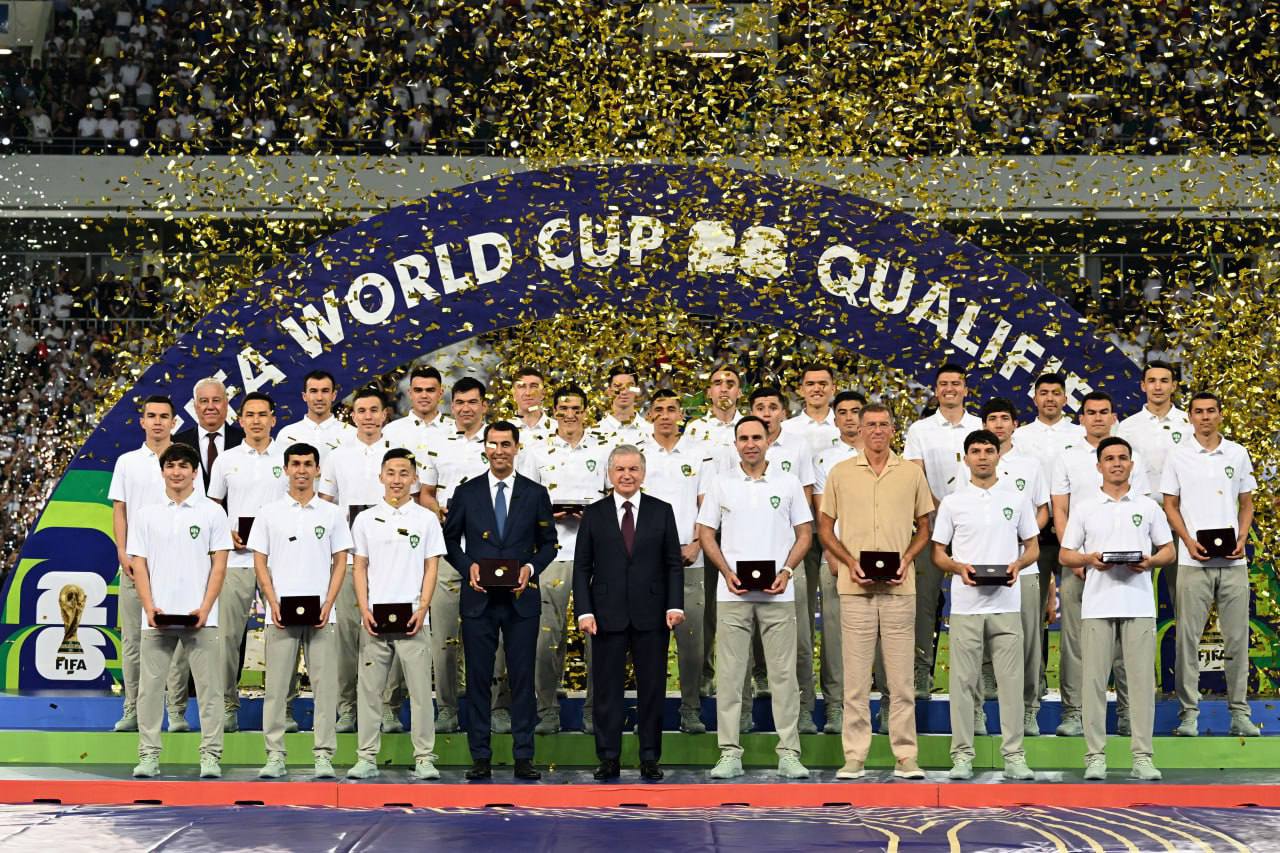 Le président ouzbek Chavkat Mirzioïev au milieu de l'équipe nationale de football, au stade Bunyodkor de Tachkent, après la qualificiation de l'Ouzbékistan au mondial 2026. Crédit : site web de la présidence.